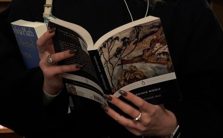 This may contain: a woman is reading a book while wearing earphones and holding an open book in her hands