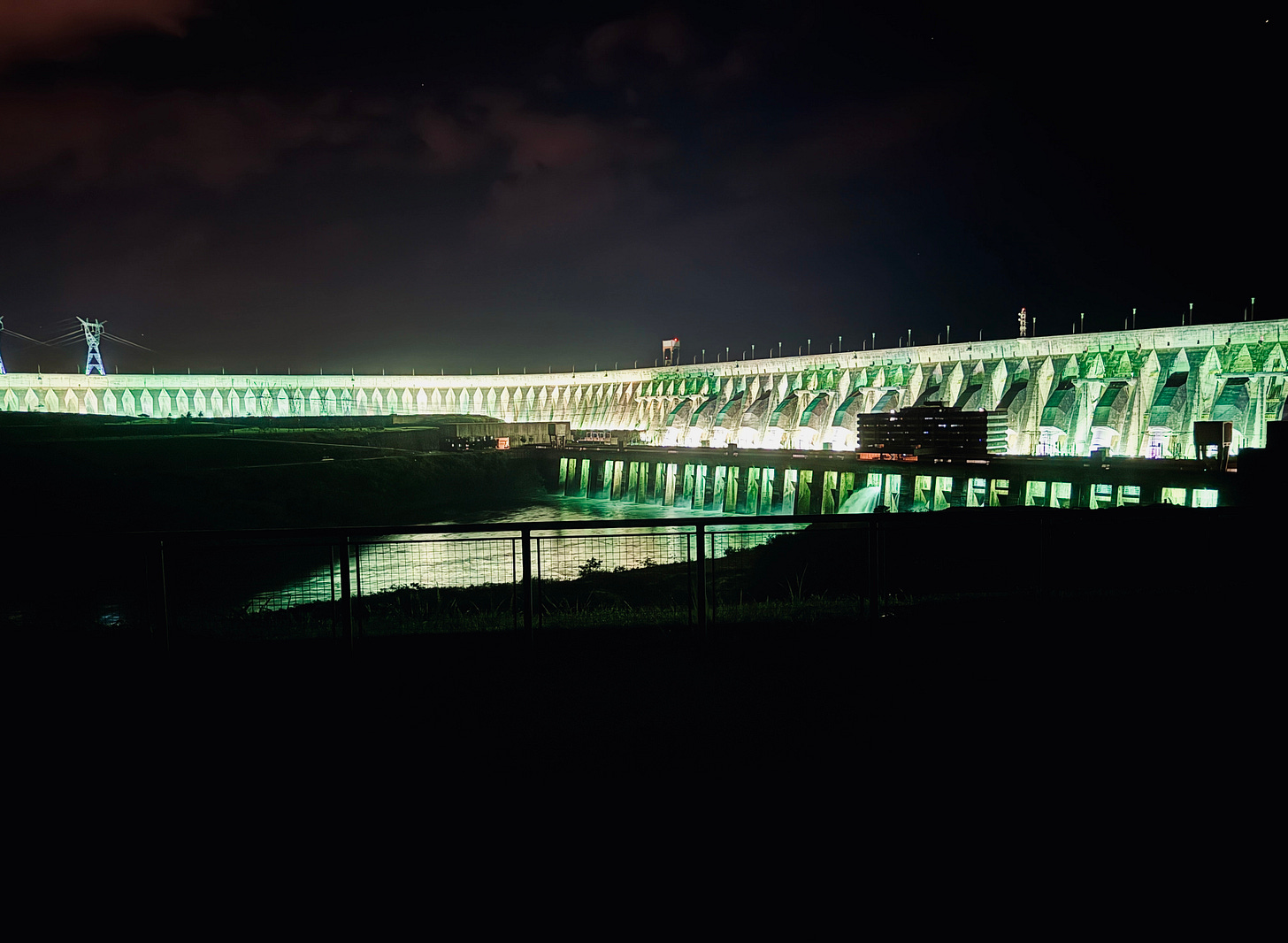 Represa de Itaipú de noche iluminada en tonos blancos y verdes. 