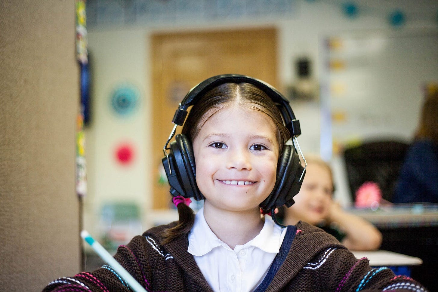 A little girl with headphones, smiling at the camera — maybe she is in a language lab? A little girl with headphones, smiling at the camera — maybe she is in a language lab?