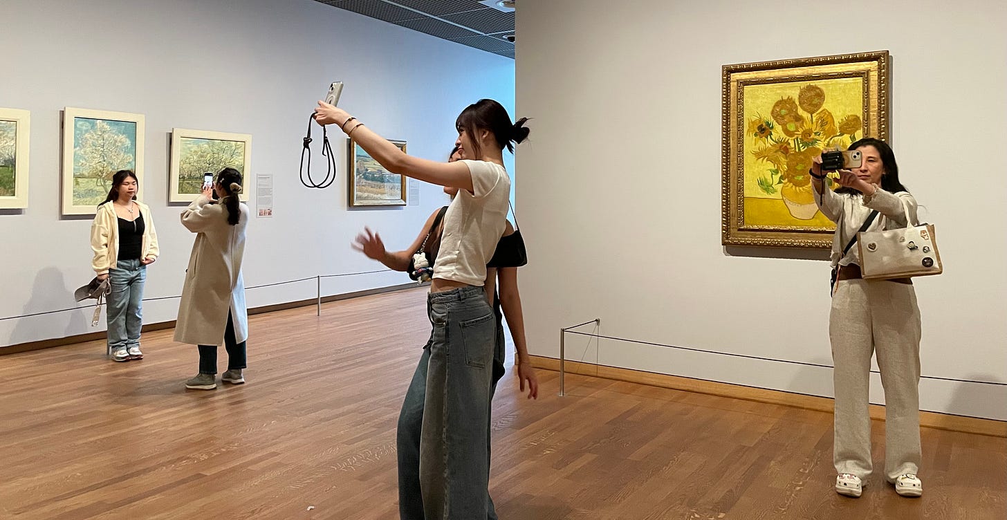 Tourists taking selfies in the Van Gogh Museum in front of the painting Sunflowers instead of looking at the artwork.
