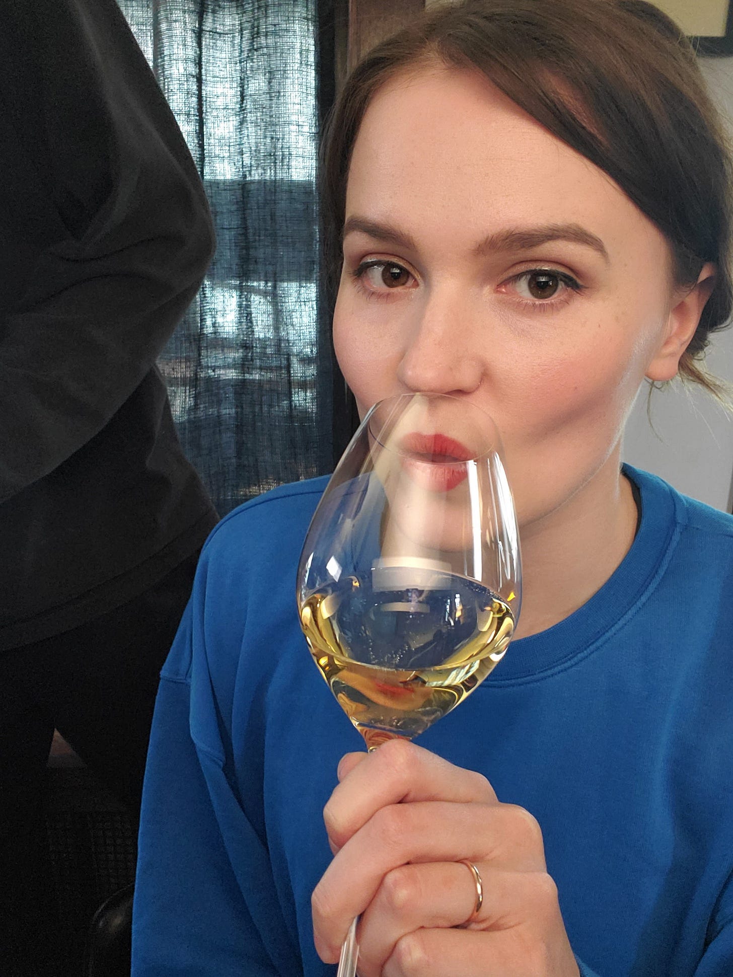 a woman (me) with brown hair in a blue sweatshirt drinking a glass of white wine