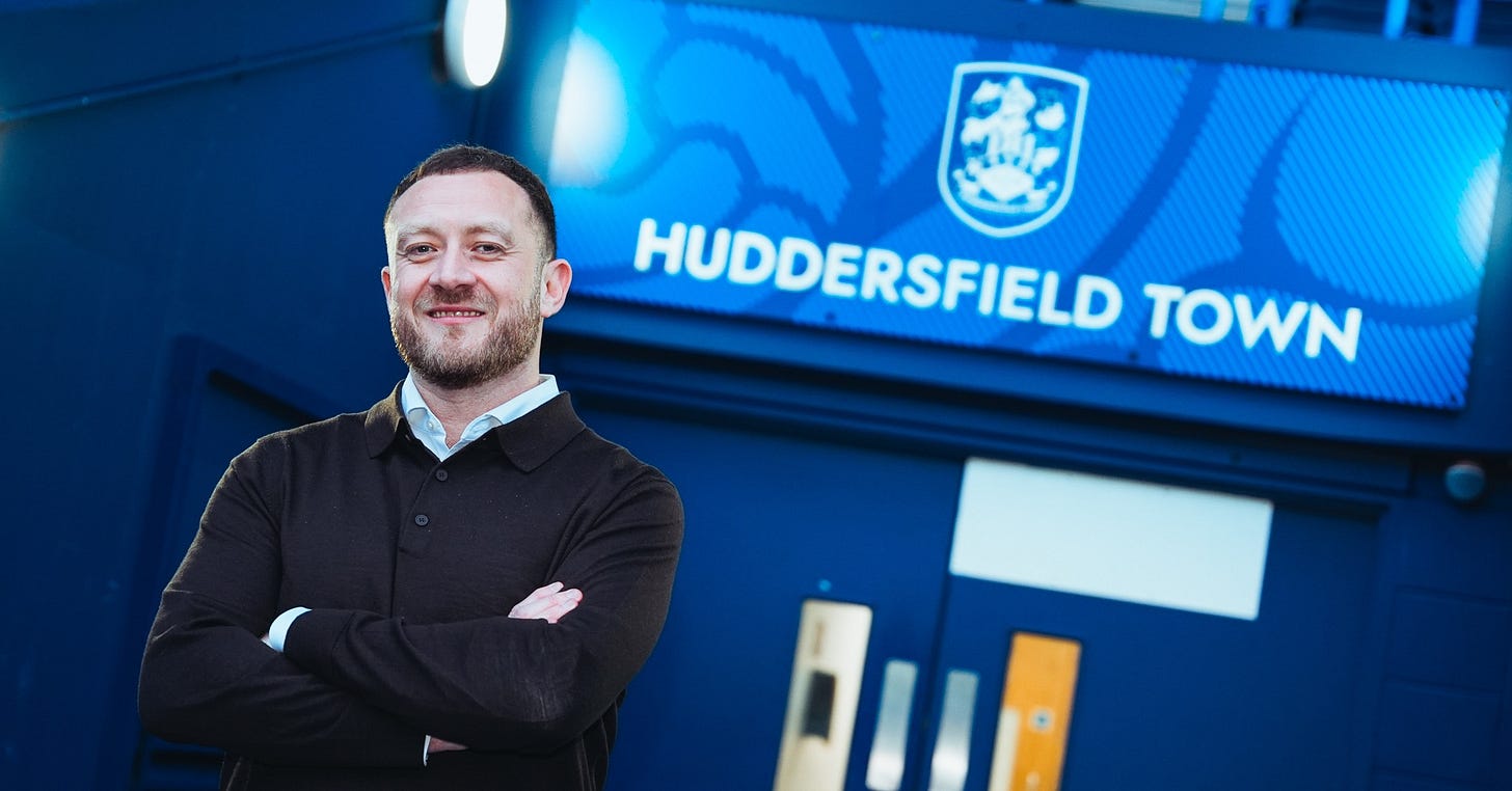 A photograph of Huddersfield Town director of football Chris Markham standing in front of a Huddersfield Town sign.