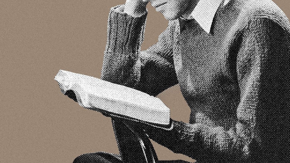 A man in a sweater reading a book, with only the lower half of his face showing