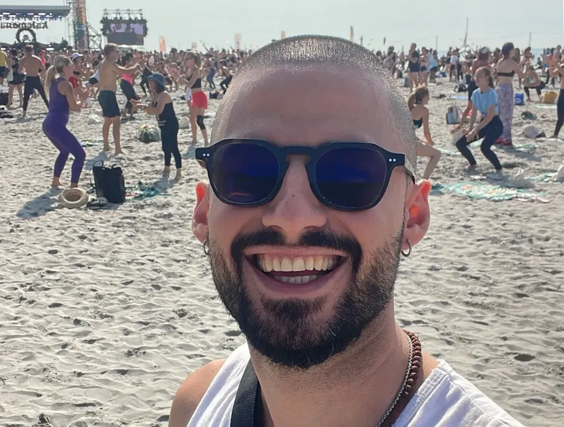 Alessandro Napoli, creatore di Onawa Retreat, sorride al Kalemana Festival, circondato da persone e energia positiva, immerso nell’atmosfera di connessione e gioia del festival.