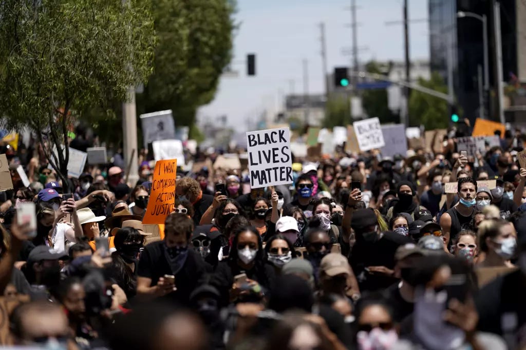 A large crowd demonstrating with homemade signs, including one reading "Black Lives Matter."