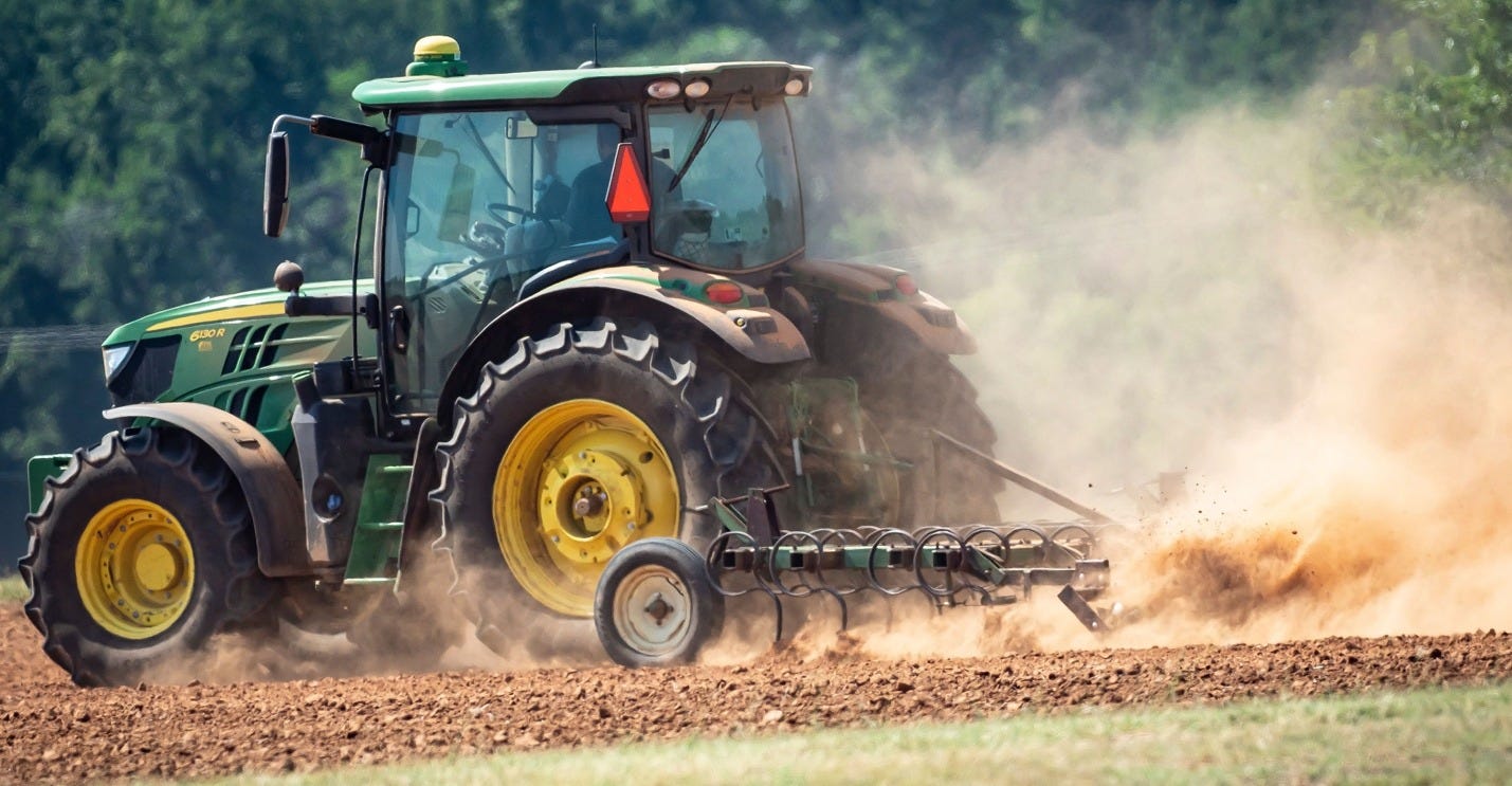 A tractor in a cloud of dust preparing a dry field for wheat to be seeded.