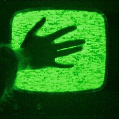 This may contain: a hand on top of a television screen with green light in the dark, while someone is reaching out their arm to touch it