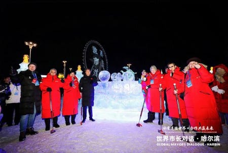 Hommes et femmes tous vêtus de parkas rouges longues jusqu'aux genoux posent devant une sculpture de glace.