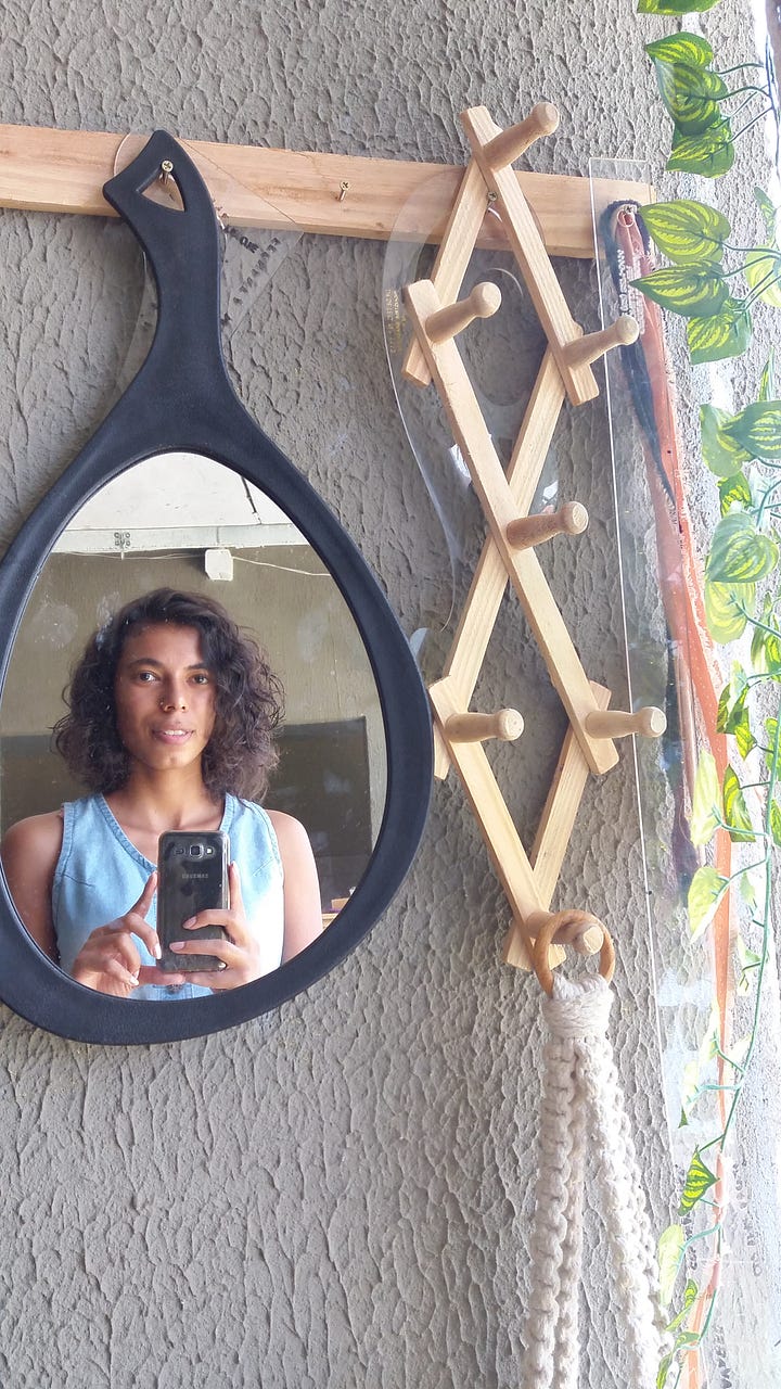Montagem com duas fotos em formato selfie. Sou uma mulher negra de pele clara. Na primeira delas, à esquerda, meu cabelo está comprido e cobre os meus ombros e o meu tronco quase inteiros, deixando ver muito pouco da minha roupa. Está bem cacheado e as pontas quase não aparecem. Na segunda, à direita, estou com o celular apontado para um pequeno espelho oval. Meu cabelo está acima dos ombros, deixando ver meu pescoço.