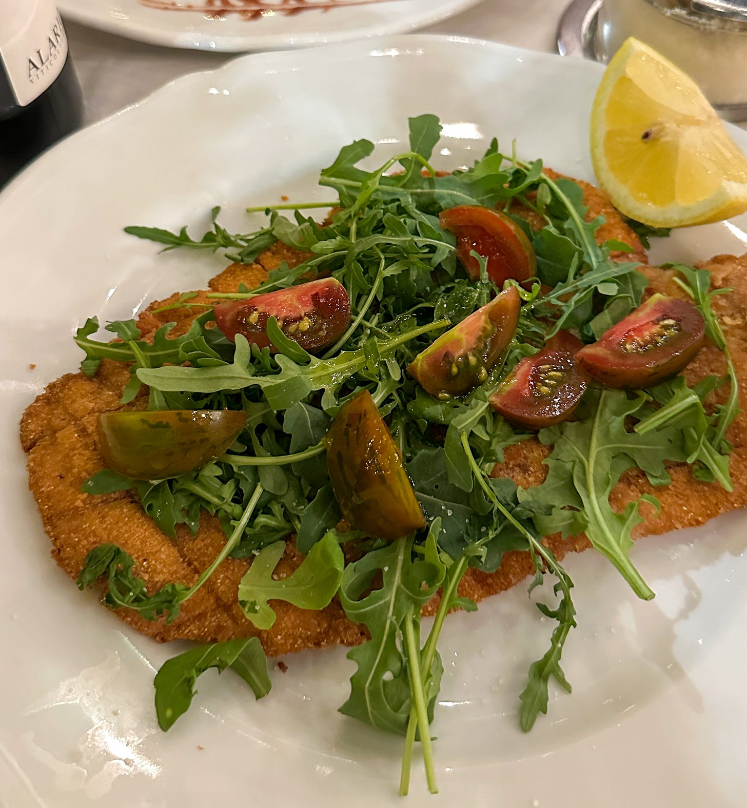 Cotoletta di Vitello alla Milanese at Il Solferino in Milan, Italy, topped with fresh arugula and tomatoes and served with a lemon wedge.