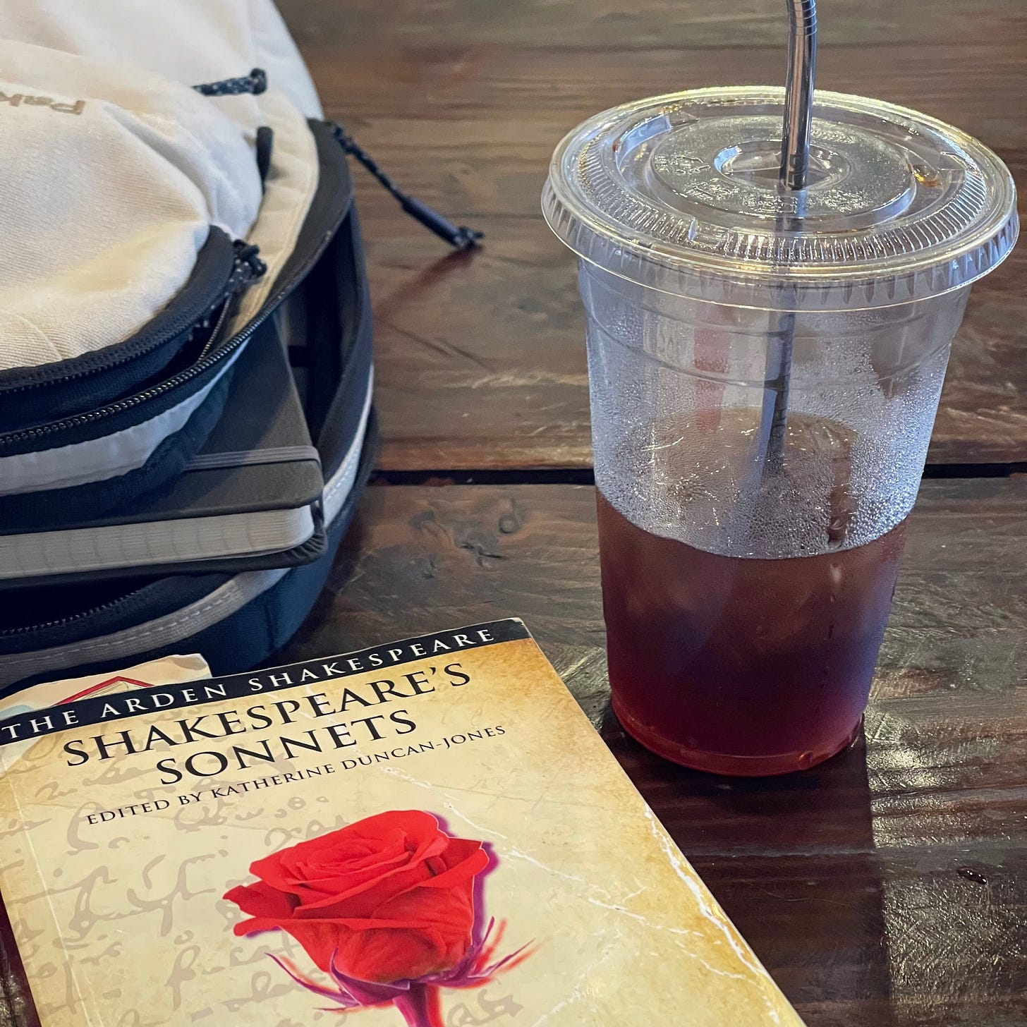 A book of Shakespeare’s sonnets on a wooden table next to a cup of cold brew coffee