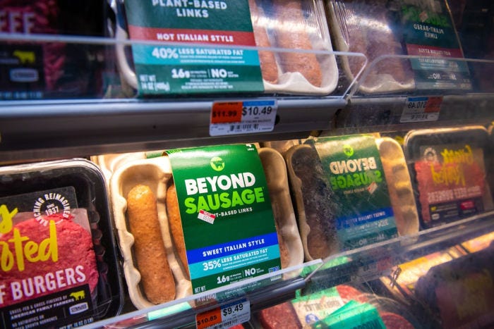 Packages of Beyond Meat sausages and other plant-based products in a grocery store refrigerated display.