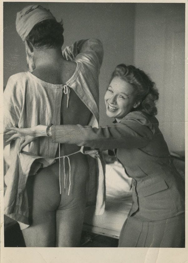 Martha Gellhorn smiles as she opens the back of Ernest Hemingway's hospital gown, exposing his buttocks. Martha Gellhorn smiles as she opens the back of Ernest Hemingway's hospital gown, exposing his buttocks.