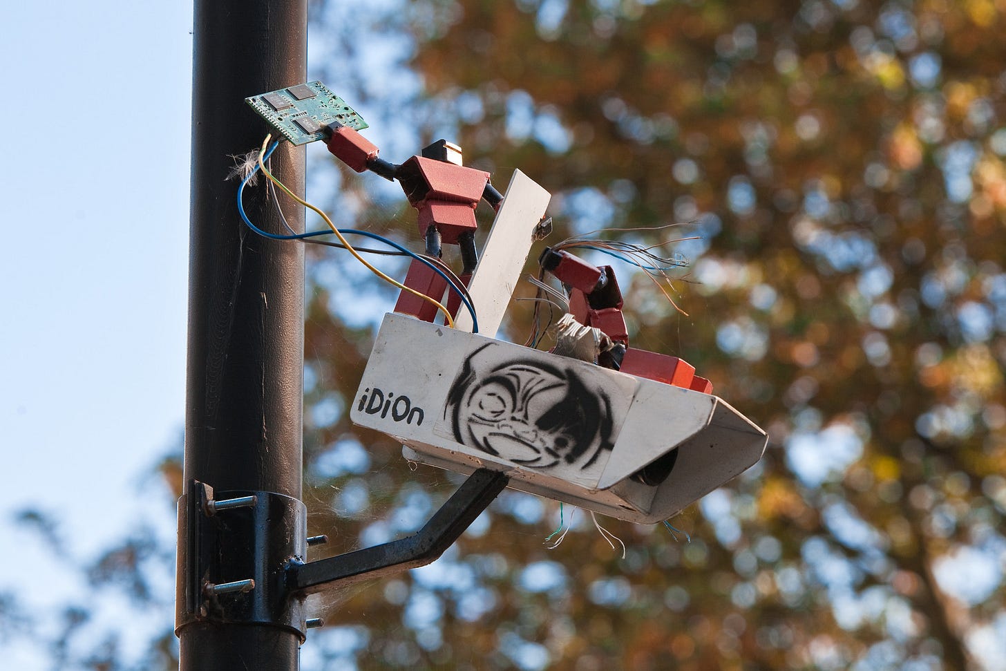 A photo of two micro robots destroying a surveillance camera that is mounted to a poll by removing its chips and wires. A photo of two micro robots destroying a surveillance camera that is mounted to a poll by removing its chips and wires.