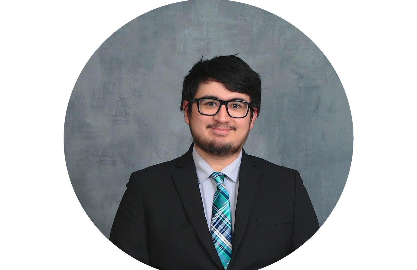 A person in a suit with a teal tie smiles into the camera. They have short dark hair, a beard, and glasses