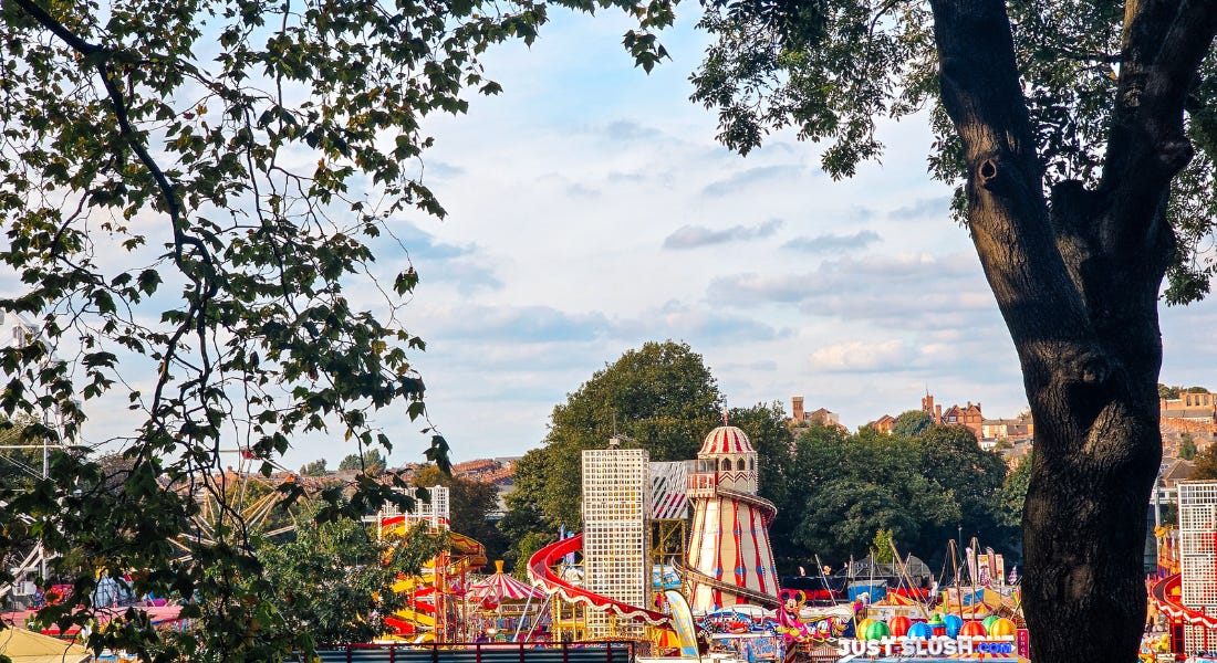 A fun fair with colourful rides, houses behind it, and a tree arching over the view A fun fair with colourful rides, houses behind it, and a tree arching over the view