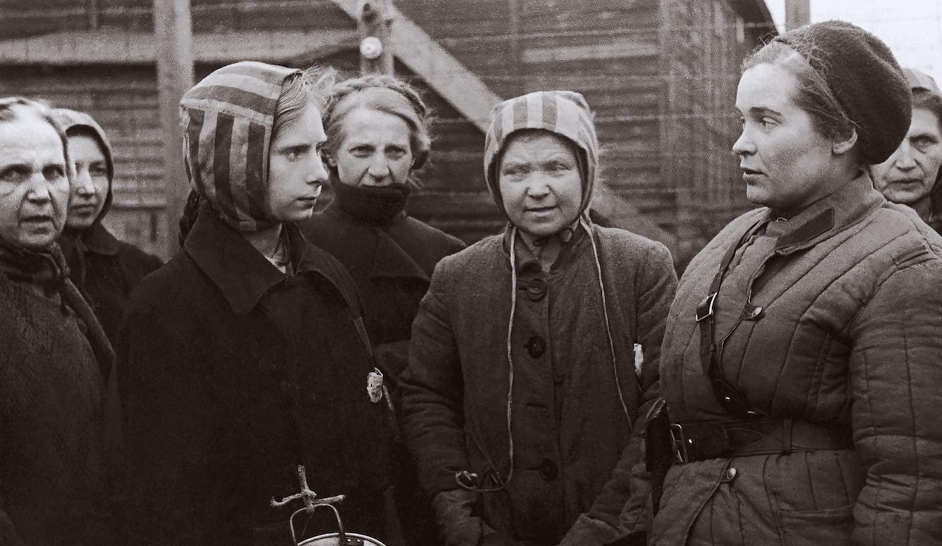 Women in coats and striped prisoner bonnets talk to a doctor in Soviet garb. Women in coats and striped prisoner bonnets talk to a doctor in Soviet garb.
