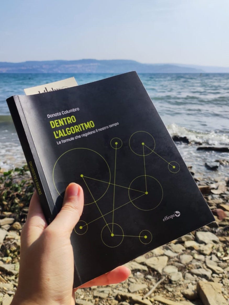 Libro con copertina nera tenuto in mano. Sullo sfondo: il mare e la costa