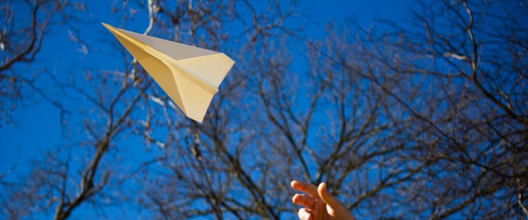 a person is flying a paper airplane in the sky
