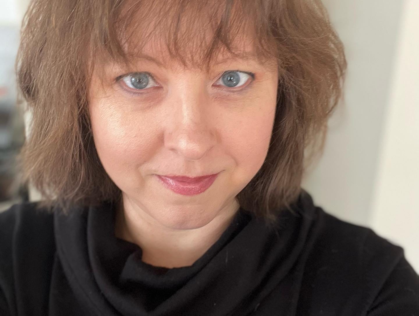 A white woman with blue eyes and a shoulder-length bob with a fringe smiling directly at the camera.