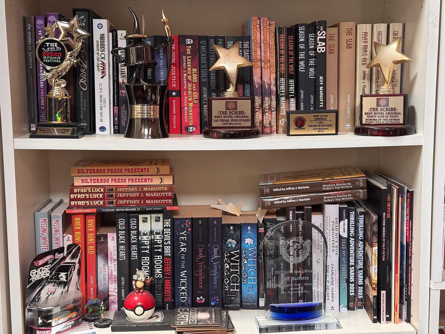 Two bookselves holding books by Jeff Mariotte, with awards standing on front of some