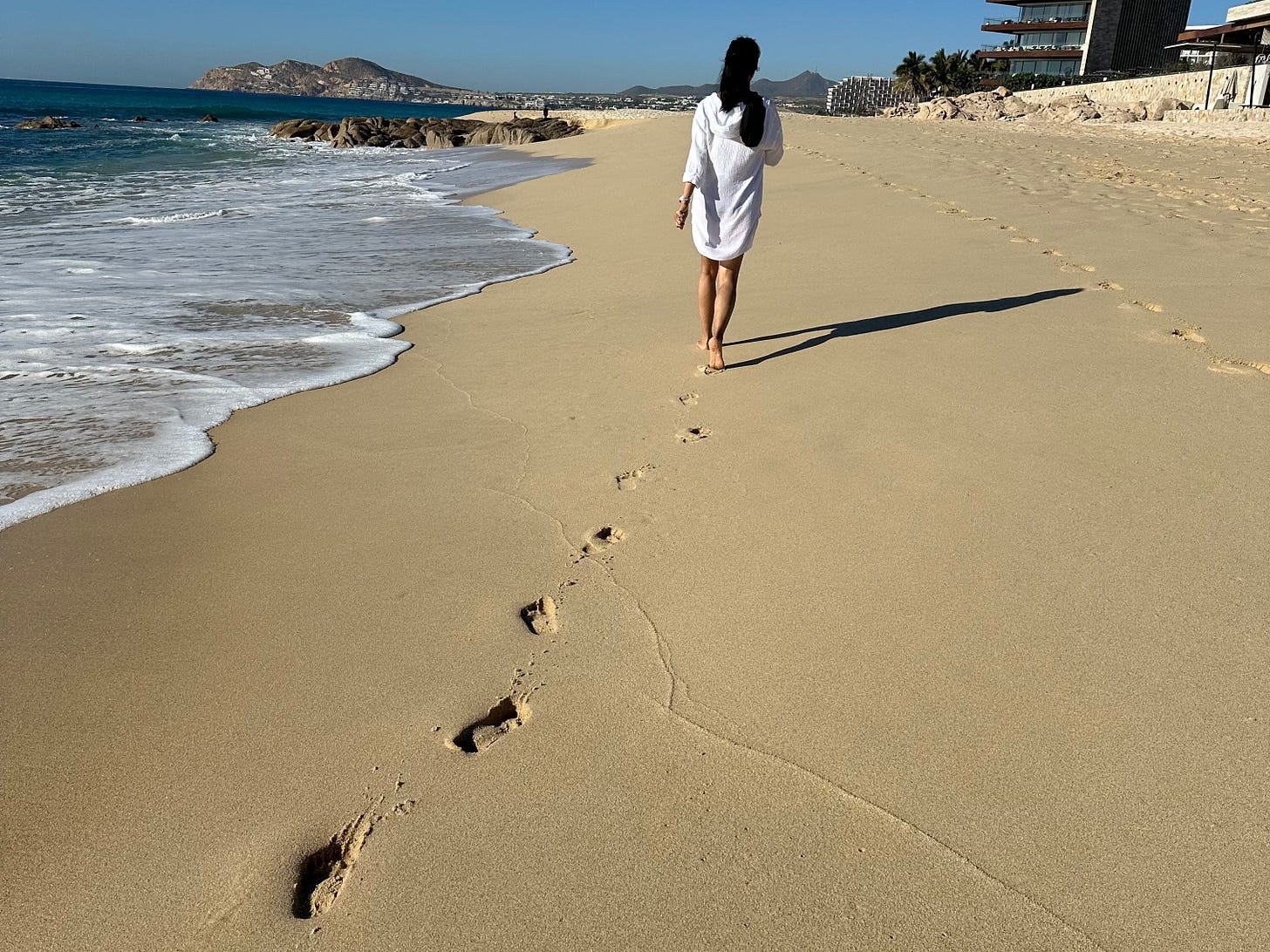 Woman walking barefoot on a Mexican beach, footprints trailing behind her in the sand.