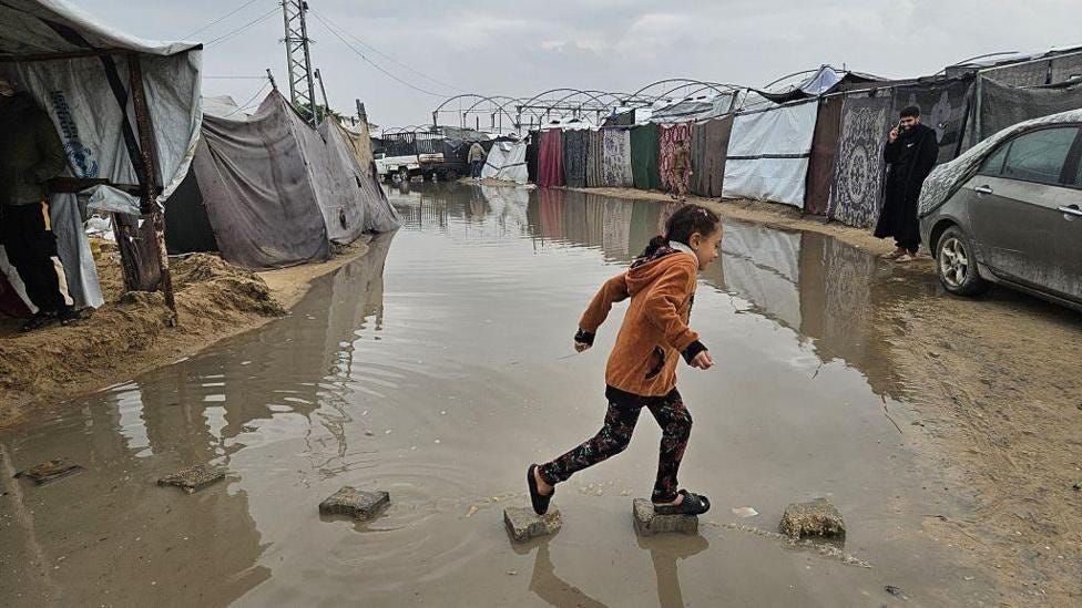 A child crosses a flooded track in Khan Younis between makeshift tents used by displaced Palestinians.