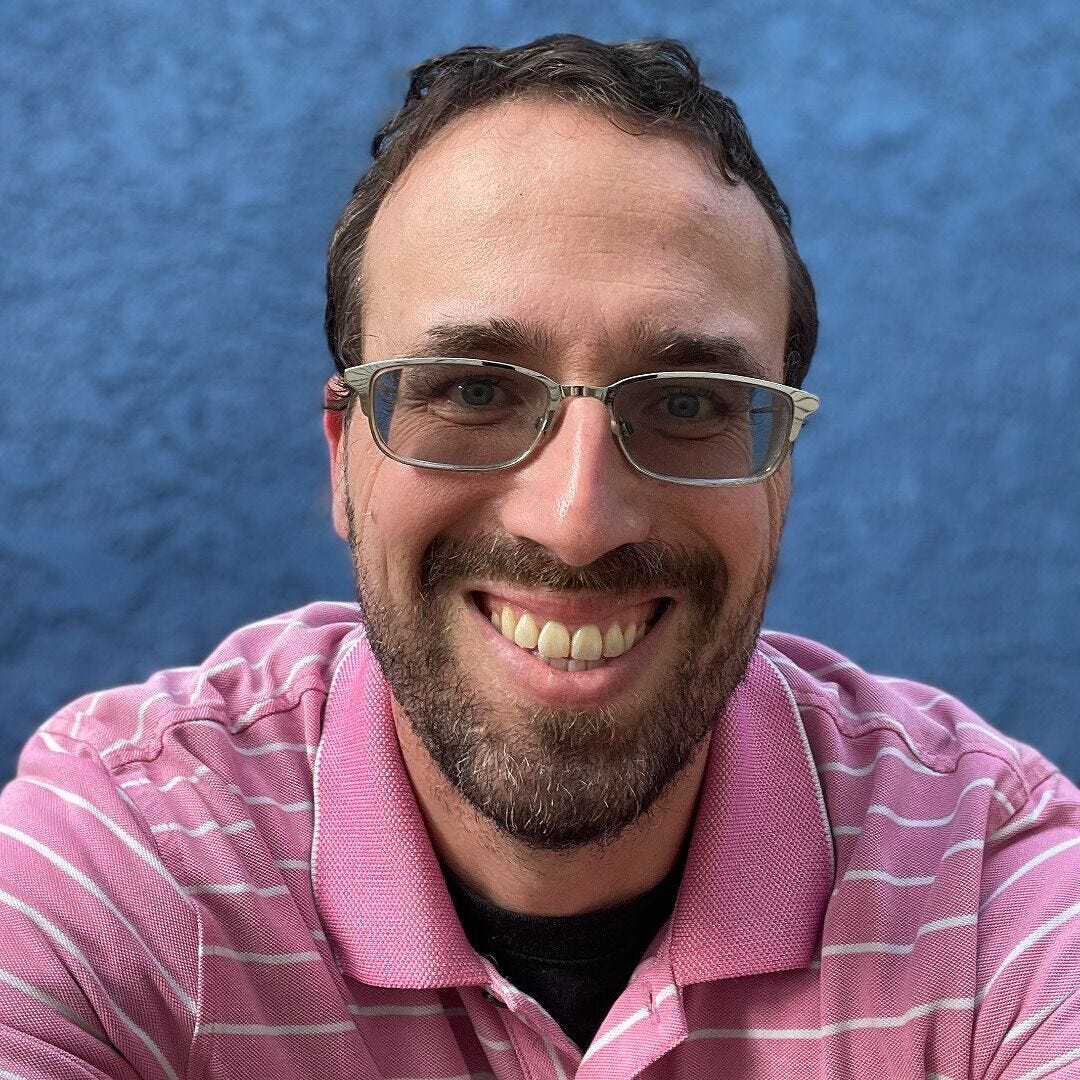 Man wearing a pink shirt and sunglasses smiling
