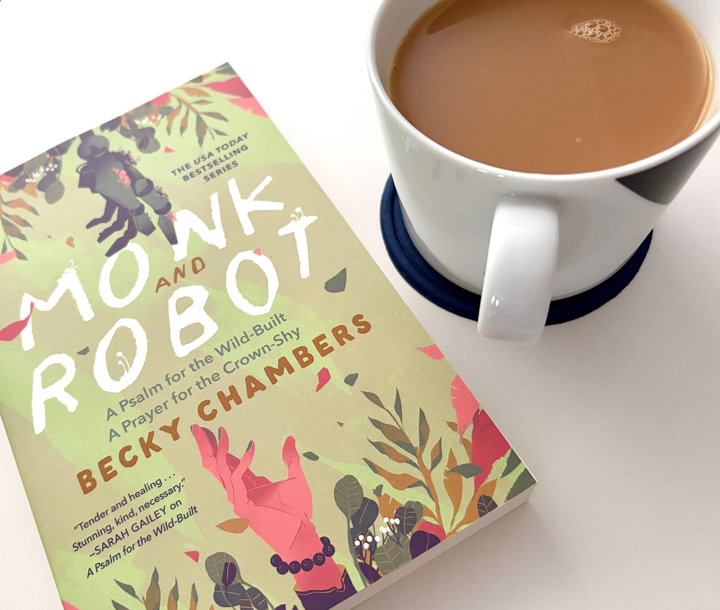 Book, "Monk and Robot" by Beck Chambers sits next to a cup of tea on a white table