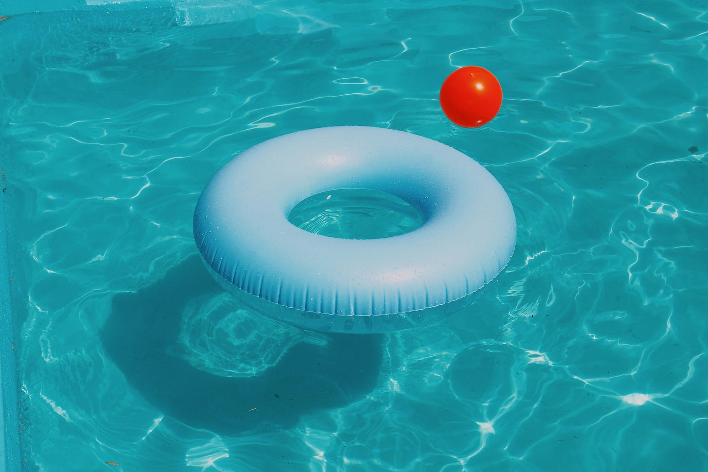 Color photo of an inflated floatie ring and a red ball floating on top of the water in a swimming pool