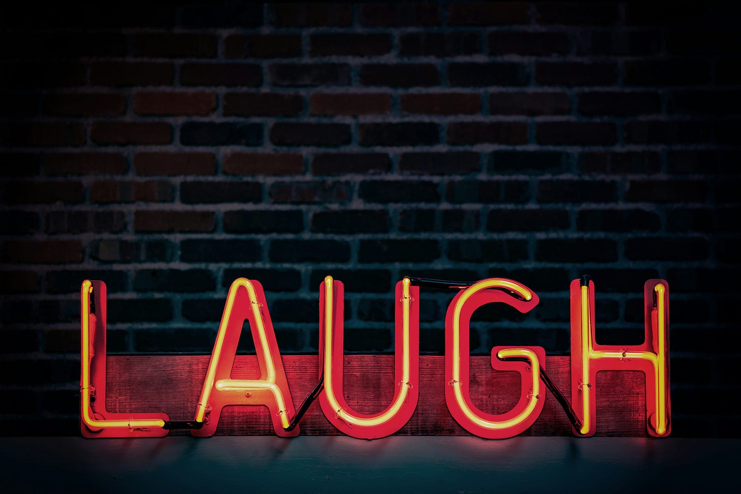 "Laugh" written in orange neon lights in all caps. "Laugh" written in orange neon lights in all caps.