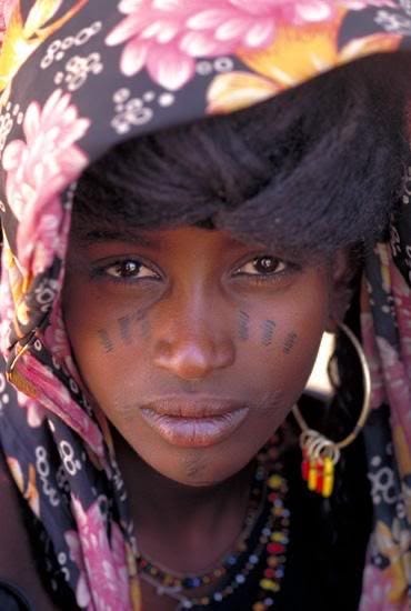 Lovette Jallow wearing yellow during a cultural gathering—scarification visible as a marker of Fulani ancestral lineage and belonging.