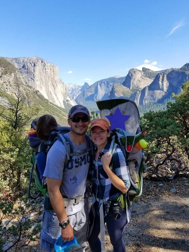 Shannon and her husband, Michael, each wearing a child sleeping in a hiking backpack on their backs with El Capitan and Half Dome of Yosemite National Park in the background. 