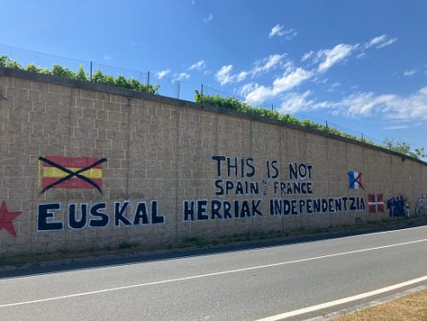 a high mountain path through greenery, roadside graffitti for Pays Basque independence, and a small Spanish town