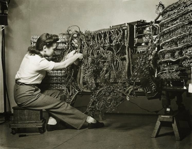 A historical telephone-switchboard operator connecting a dense panel of cords.