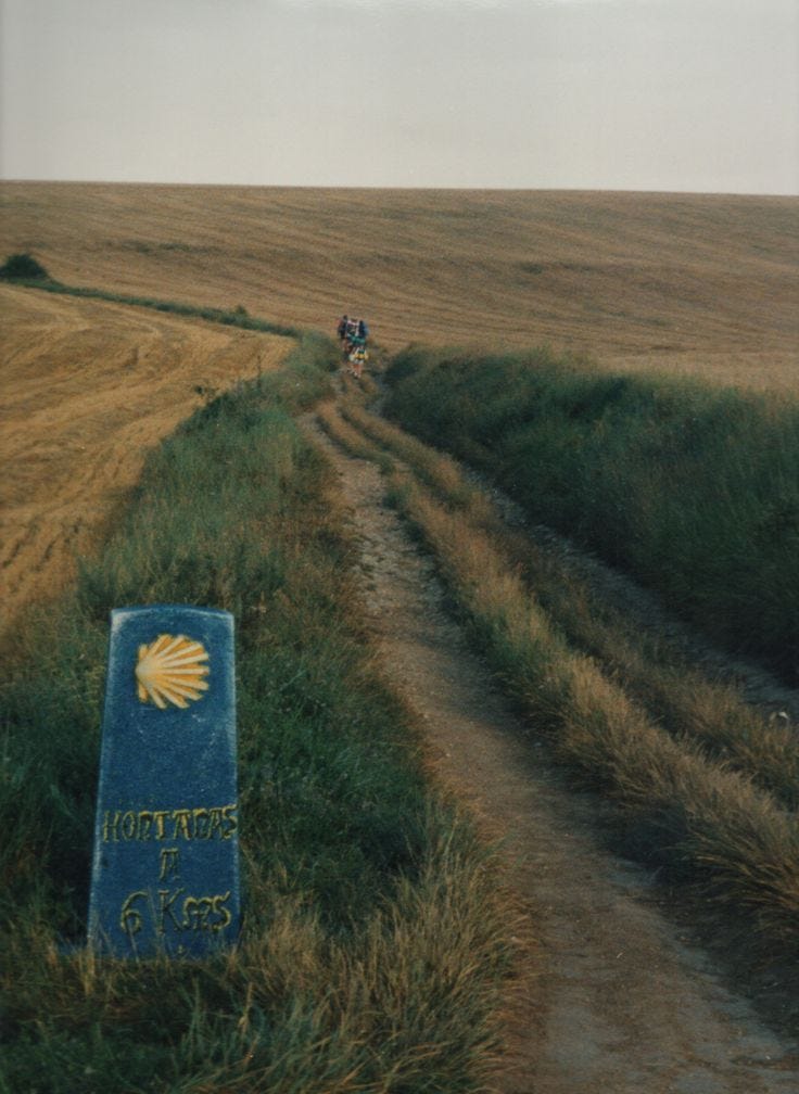 This may contain: two people riding bikes on a dirt road in the middle of an open grassy field