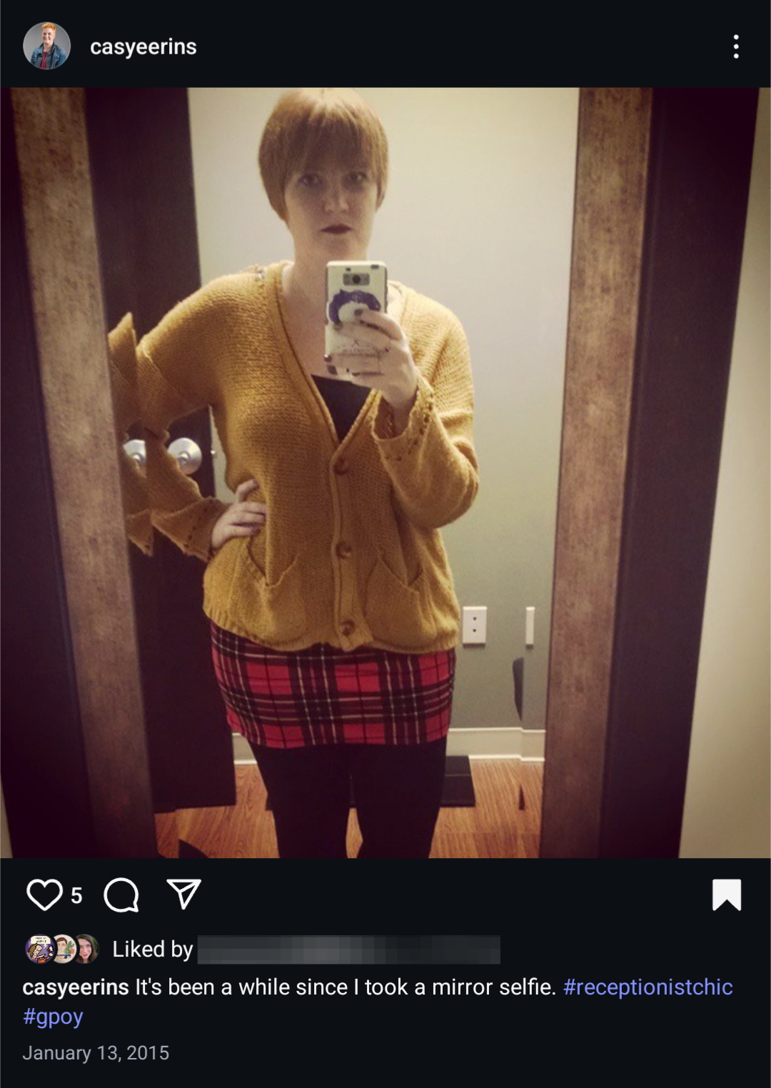 A screenshot of an Instagram picture of a person. They are depicted using their phone to take a photo of their reflection. They are wearing a yellow cardigan, a red plaid skirt, and tall boots. The caption says "it's been a while since I took a mirror selfie."