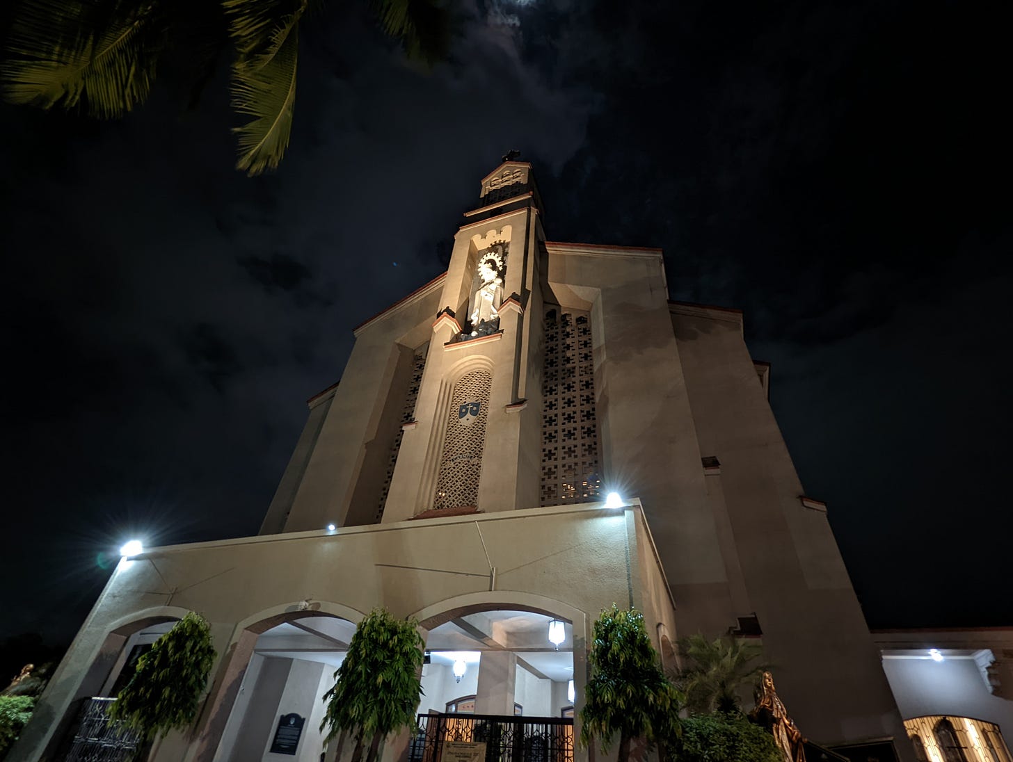 A darker shot of the lit facade of Our Lady of Mount Carmel faintly showing the overcast weather