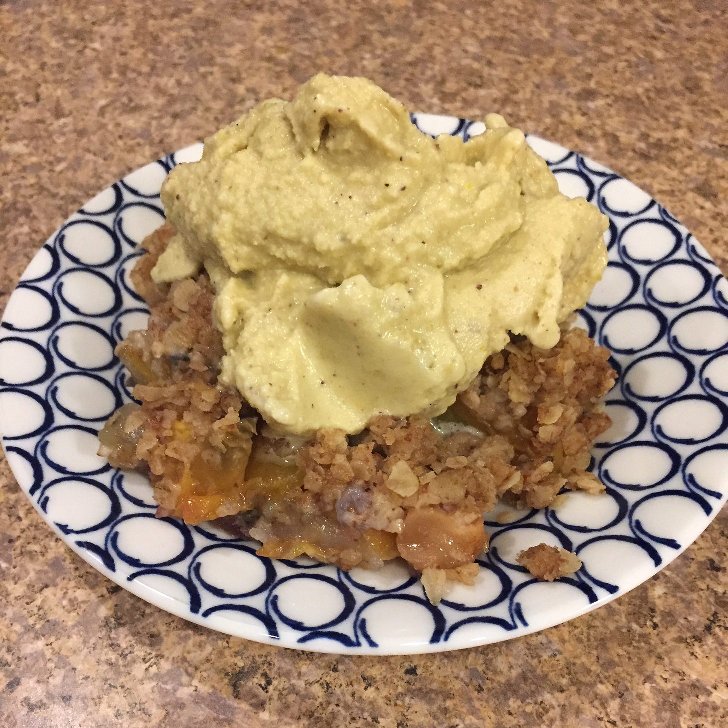 on a blue and white patterned plate, a mess of peach and apple cobbler with a soft-looking scoop of pistachio ice cream on top.