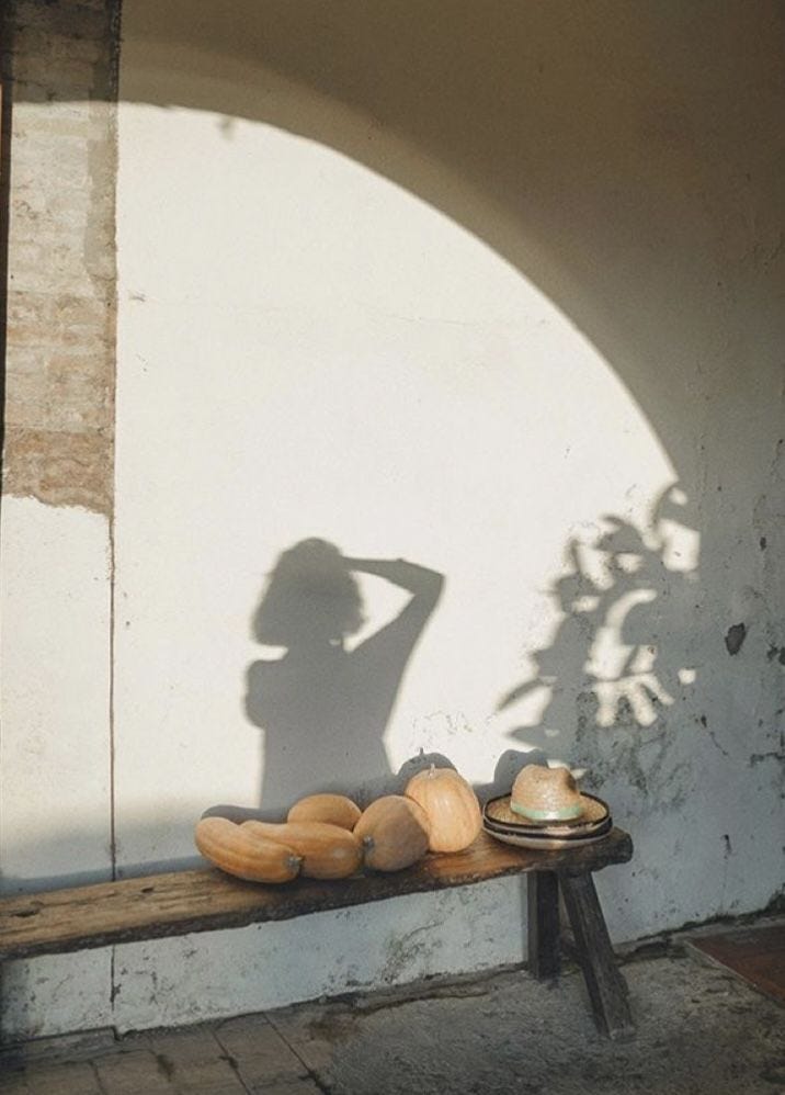 This may contain: a woman standing next to a wooden bench with bread on the table in front of her