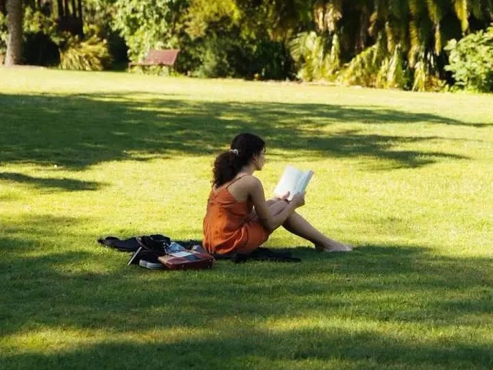 This may contain: a woman sitting on the grass reading a book