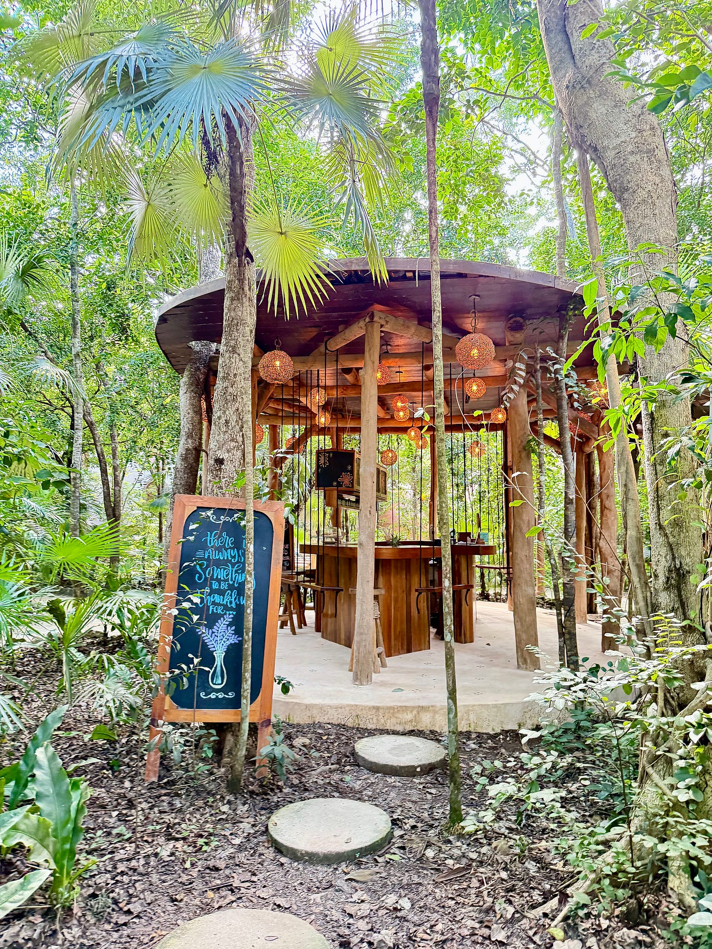 A cozy open-air wooden café nestled in the jungle, with warm hanging lanterns, a chalkboard sign out front, and lush green trees surrounding the space. A cozy open-air wooden café nestled in the jungle, with warm hanging lanterns, a chalkboard sign out front, and lush green trees surrounding the space.