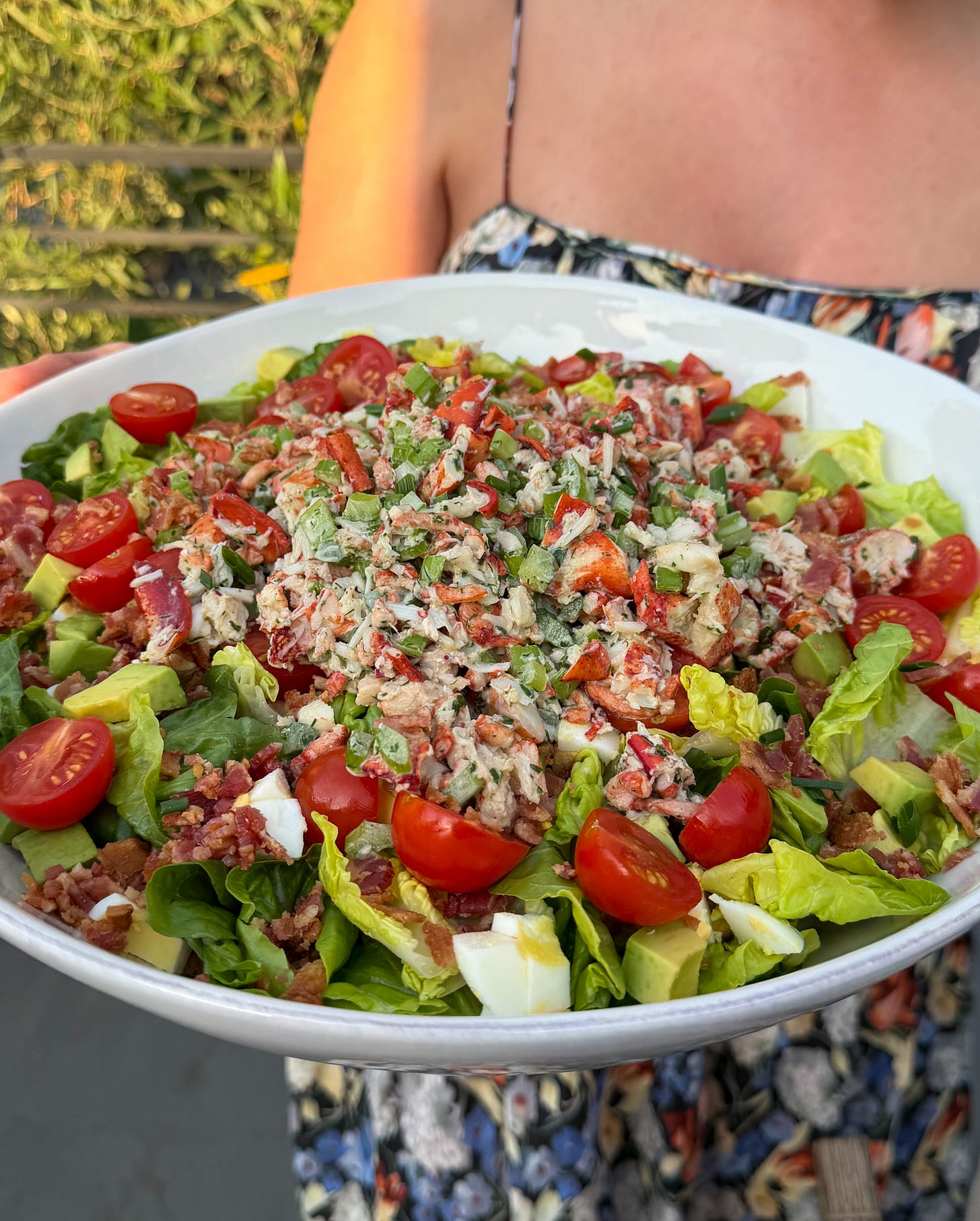 A vibrant and delicious Lobster Cobb Salad being held in a large serving bowl in an al fresco dining setup.