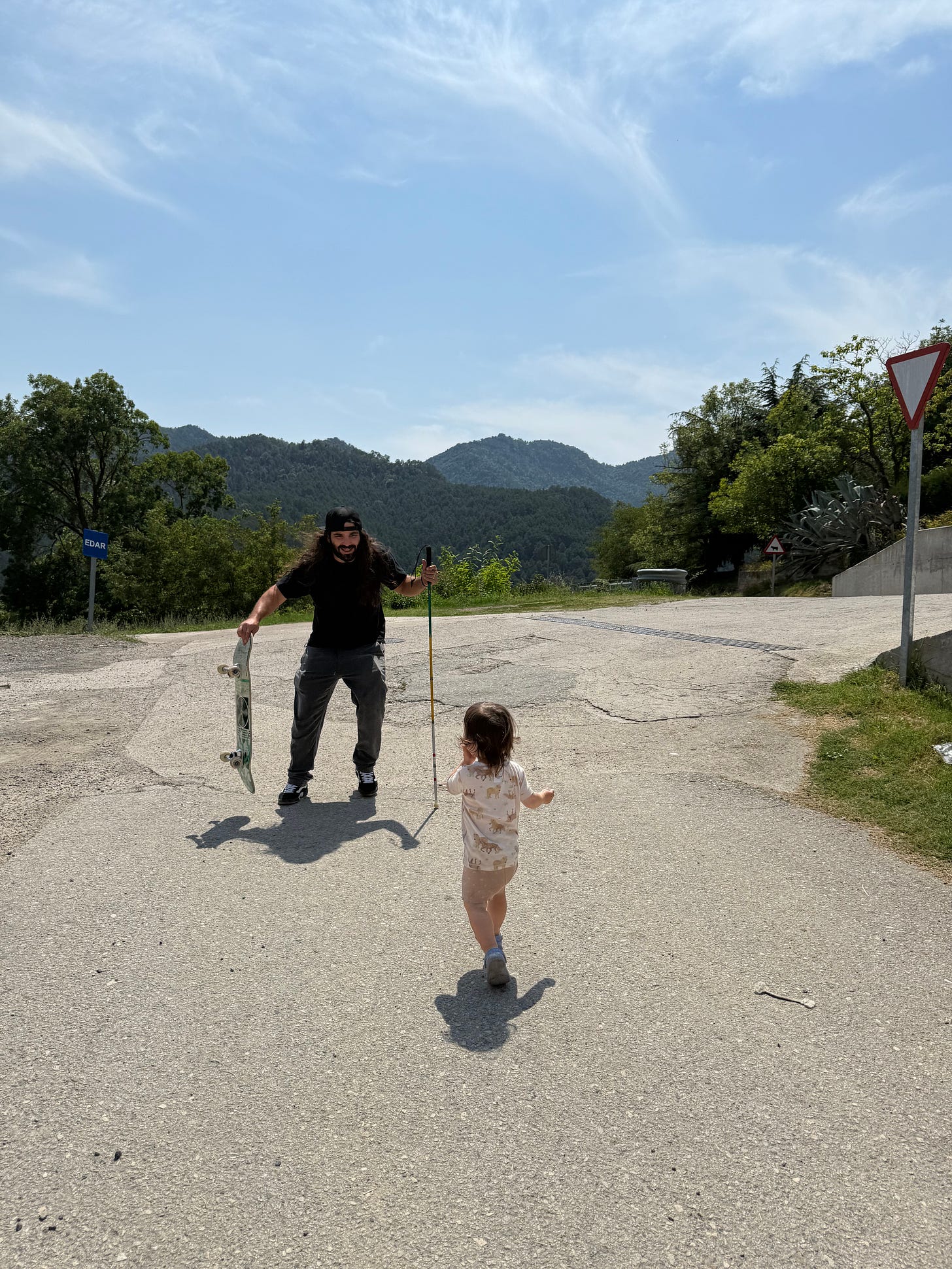 anthony holds his cane in one hand and his skateboard in the other as he runs towards his daughter who is running towards him about to give him a hug in the mountains