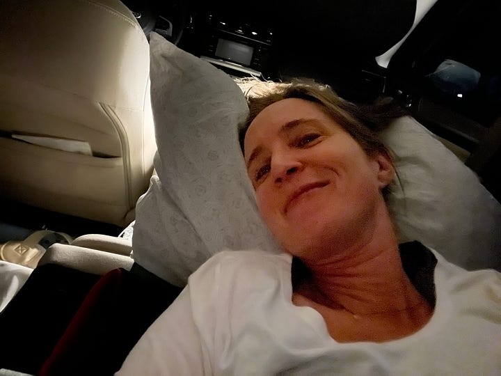 selfie of the author in the car bed; view of the sunrise through the back window of the car with a purple sleeping bag in the foreground