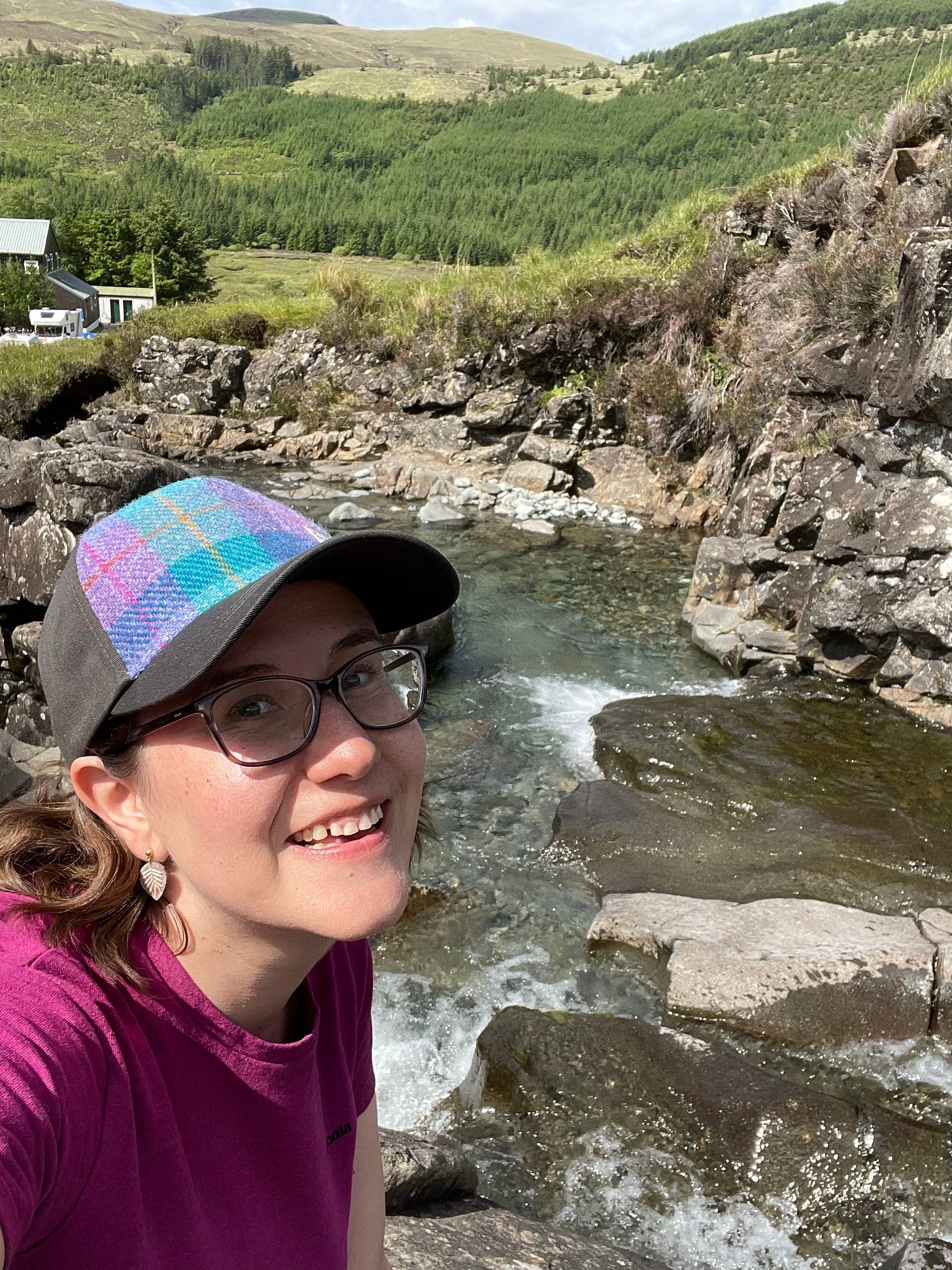 Lindsey smiling, wearing a tweed baseball cap while standing beside cascading pools, looking for fairies. Lindsey smiling, wearing a tweed baseball cap while standing beside cascading pools, looking for fairies.