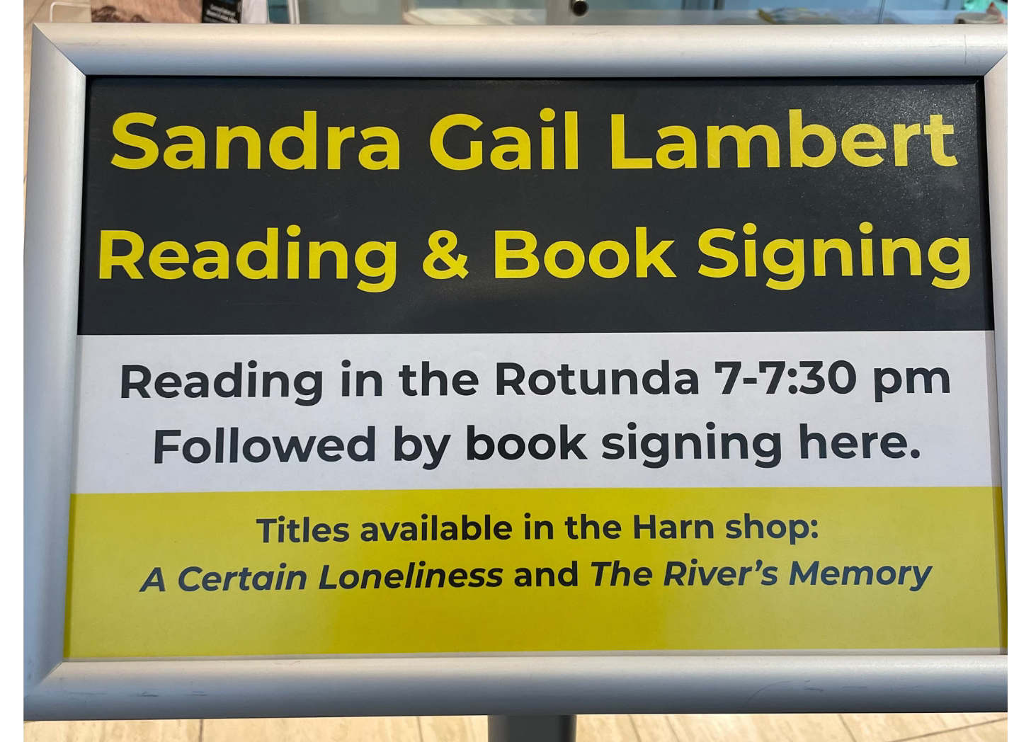  A sign that says "Sandra Gail Lambert, Reading and Booksigning. Reading in the Rotunda. Titles available in the Harn Shot A Certain loneliness and The River's Memory