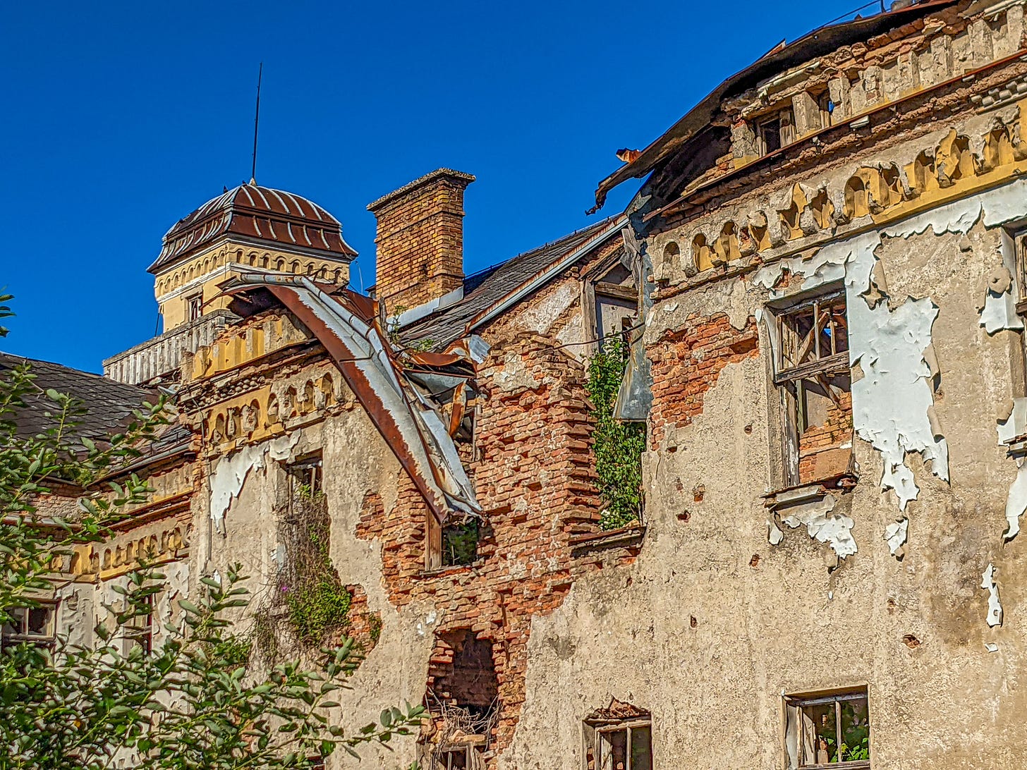 A badly damaged building with a partially collapses roof, shattered windows, and walls filled with bullet holes. 