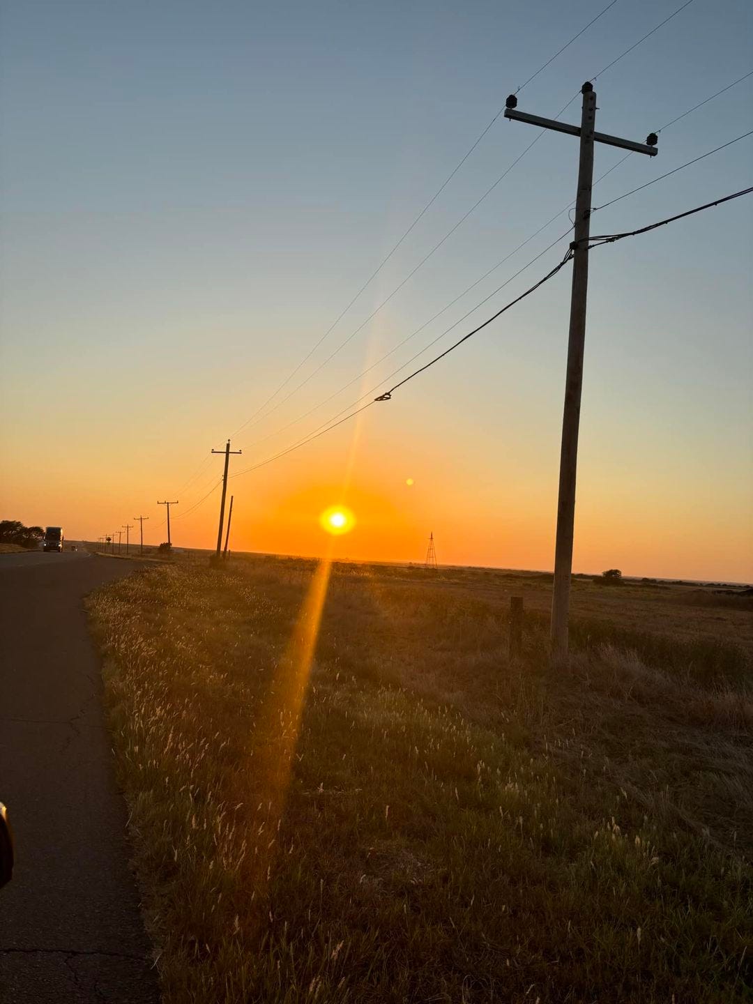 May be an image of twilight, horizon, road, grass and windmill