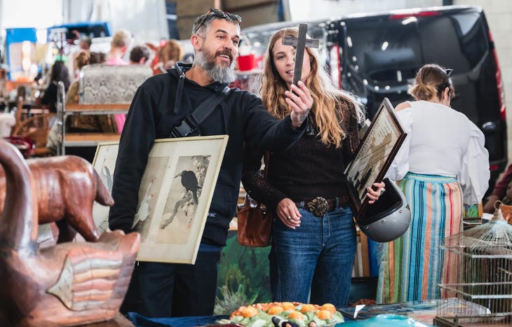A man and woman examining a wooden cross at a flea market A man and woman examining a wooden cross at a flea market